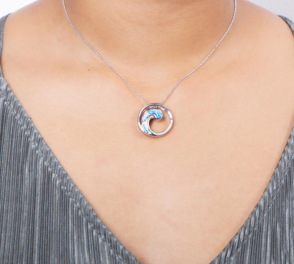 In this photo there is a model with a gray shirt wearing a sterling silver circle and wave pendant with blue opalite and topaz gemstones.