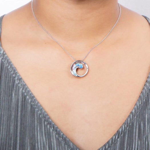 In this photo there is a model with a gray shirt wearing a sterling silver circle and wave pendant with blue opalite and topaz gemstones.
