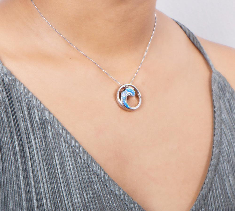 In this photo there is a model with a gray shirt turned slightly to the right, wearing a sterling silver circle and wave pendant with blue opalite and topaz gemstones.