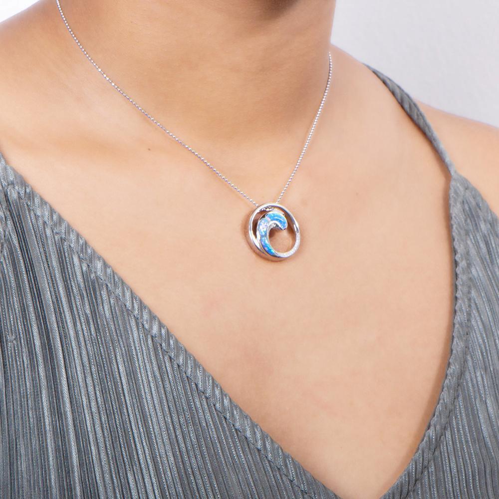 In this photo there is a model with a gray shirt turned slightly to the right, wearing a sterling silver circle and wave pendant with blue opalite and topaz gemstones.