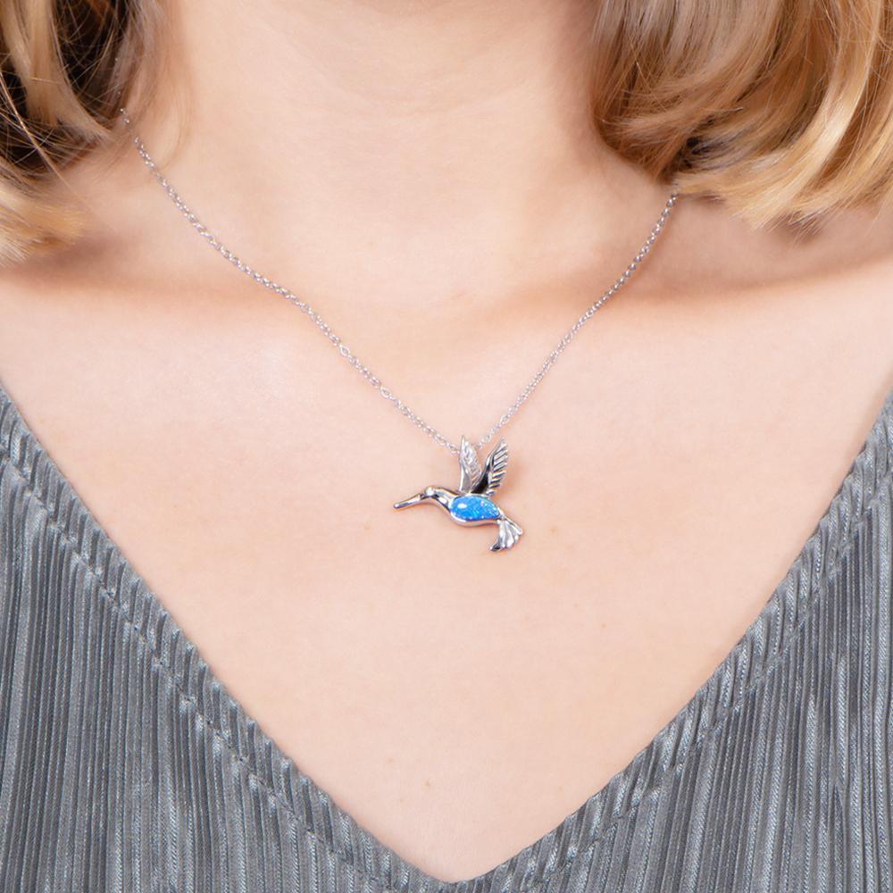 In this photo there is a model with blonde hair and a gray shirt, wearing a sterling silver hummingbird pendant with topaz and blue opalite gemstones.