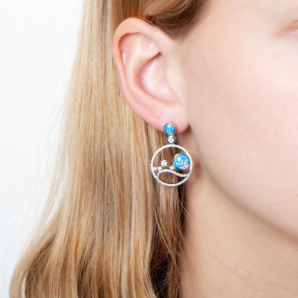 In this photo there is a close-up of a model with blonde hair, wearing sterling silver circle earrings with blue opalite, aquamarine, and cubic zirconia.