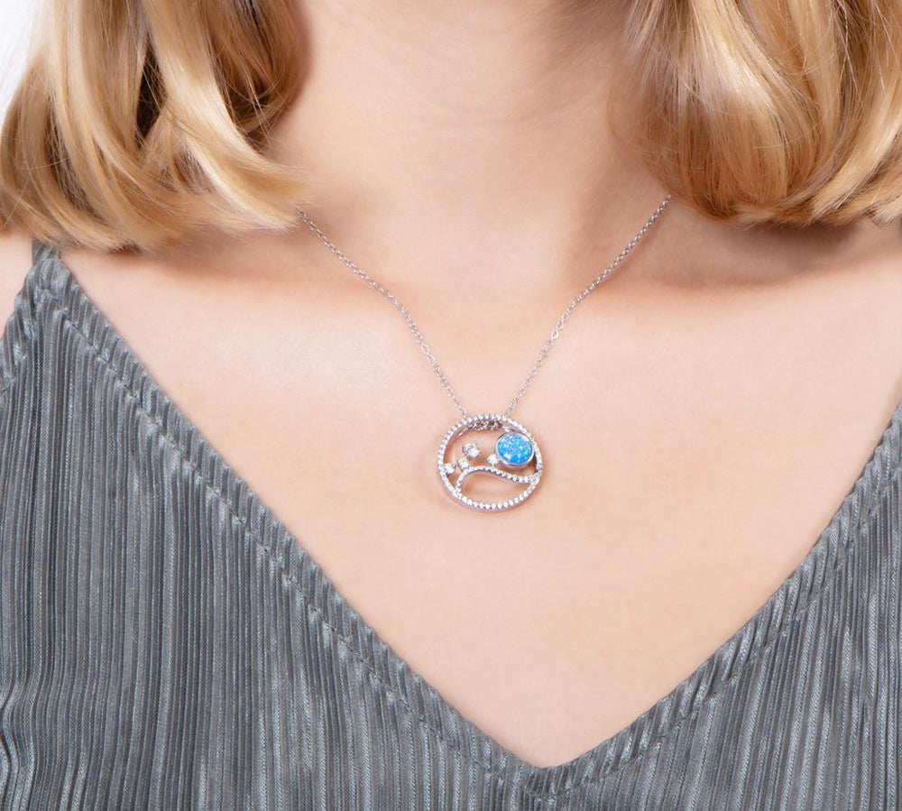 In this photo there is a model with blonde hair and a gray shirt wearing a sterling silver circle pendant with blue opalite, aquamarine and cubic zirconia.
