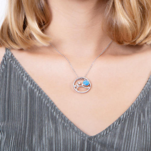 In this photo there is a model with blonde hair and a gray shirt wearing a sterling silver circle pendant with blue opalite, aquamarine and cubic zirconia.