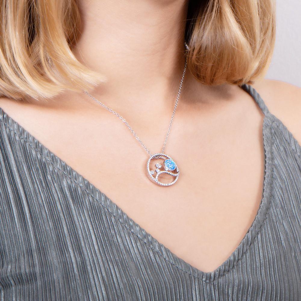 In this photo there is a model turned to the right with blonde hair and a gray shirt wearing a sterling silver circle pendant with blue opalite, aquamarine and cubic zirconia.