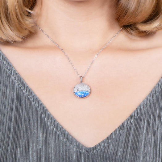 In this photo there is a model with blonde hair and a gray shirt, wearing a sterling silver lighthouse medallion pendant with blue opalite and topaz gemstones.
