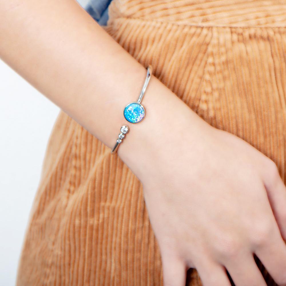 The picture shows a model wearing a 925 sterling silver opalite lunar orbit bangle with three topaz gemstones.