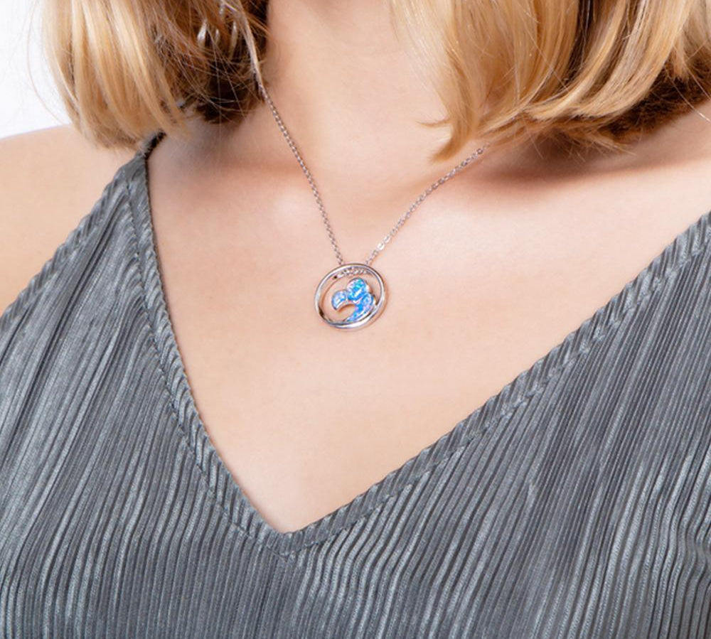 In this photo there is a model with blonde hair and a gray shirt, wearing a sterling silver big wave circle pendant with blue opalite gemstones. 