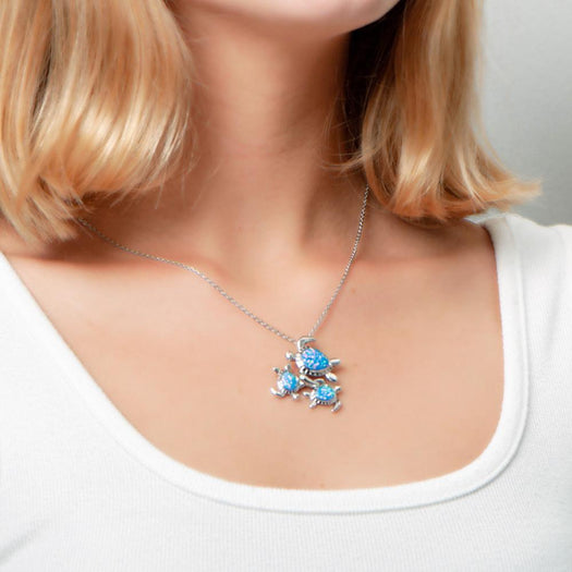 The picture shows a model wearing a 925 sterling silver opalite family of three sea turtles pendant with topaz.