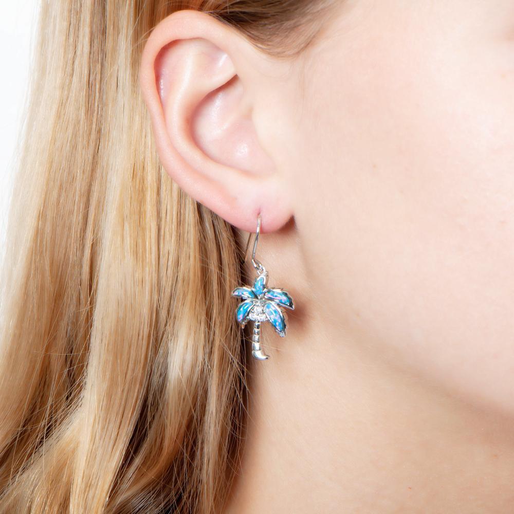 In this picture there is a close up of a model turned to the right, wearing a palm tree earring with blue opalite and topaz gemstones set in sterling silver.