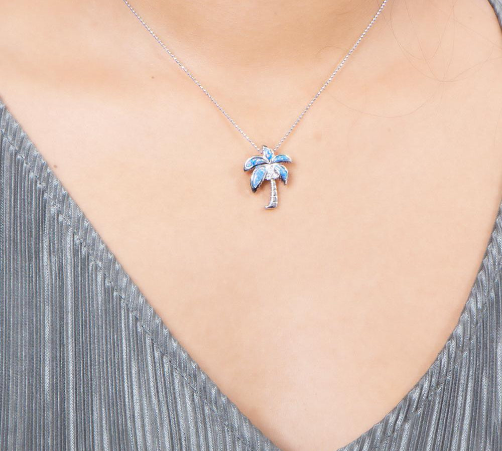 In this photo there is a model with a gray shirt wearing a sterling silver palm tree pendant with blue opalite and three topaz gemstones.