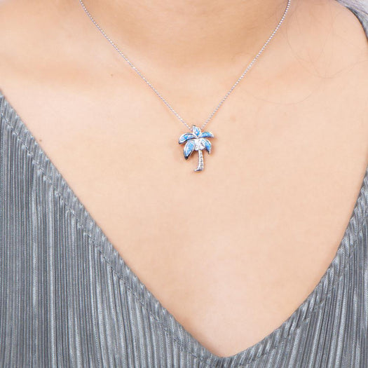 In this photo there is a model with a gray shirt wearing a sterling silver palm tree pendant with blue opalite and three topaz gemstones.