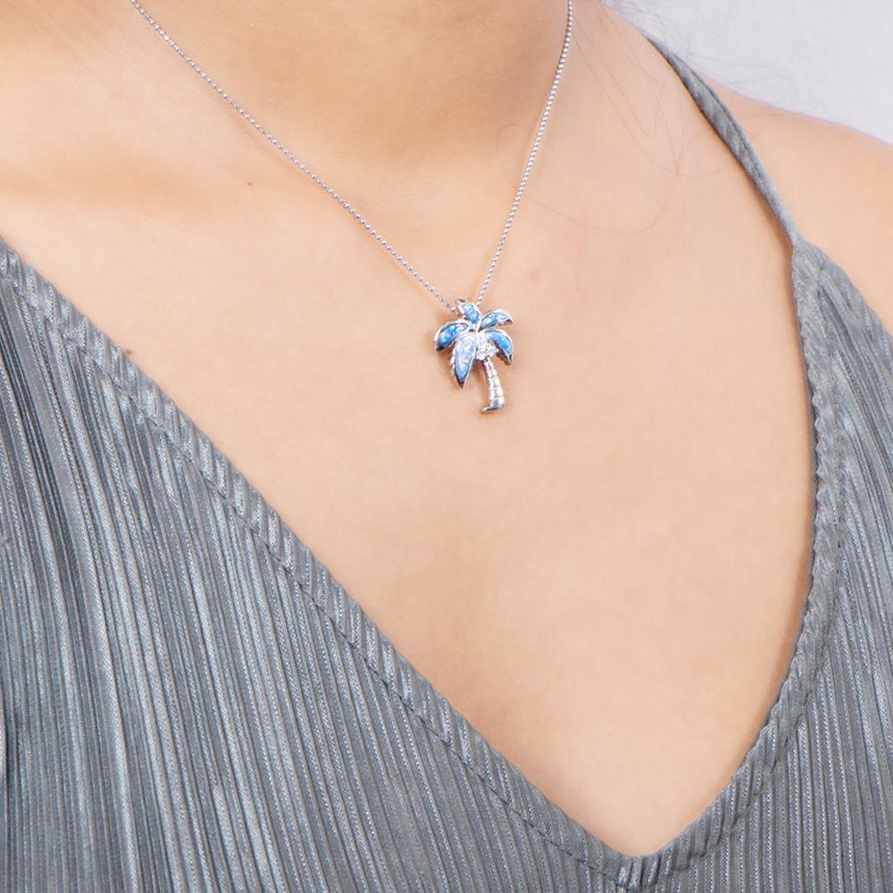 In this photo there is a model with a gray shirt turned slightly to the right, wearing a sterling silver palm tree pendant with blue opalite and three topaz gemstones.