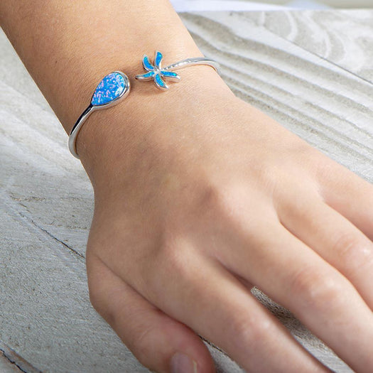 In this photo there is a close up of a model wearing a sterling silver palm tree and teardrop bangle with blue opalite gemstones on her left wrist.