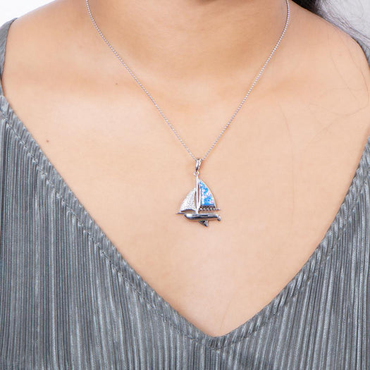 In this photo there is a model with a gray shirt wearing a sterling silver sailboat pendant with blue opalite and topaz gemstones.