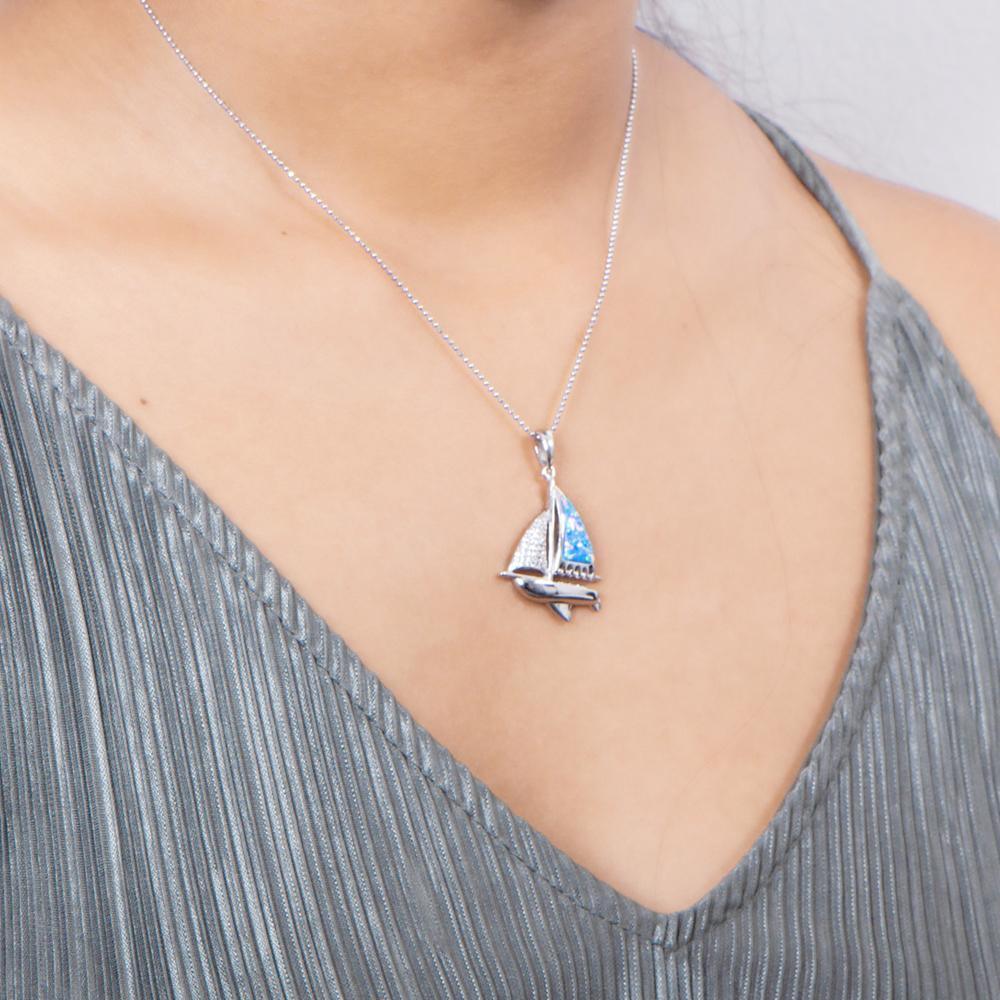 In this photo there is a model with a gray shirt turned slightly to the right, wearing a sterling silver sailboat pendant with blue opalite and topaz gemstones.