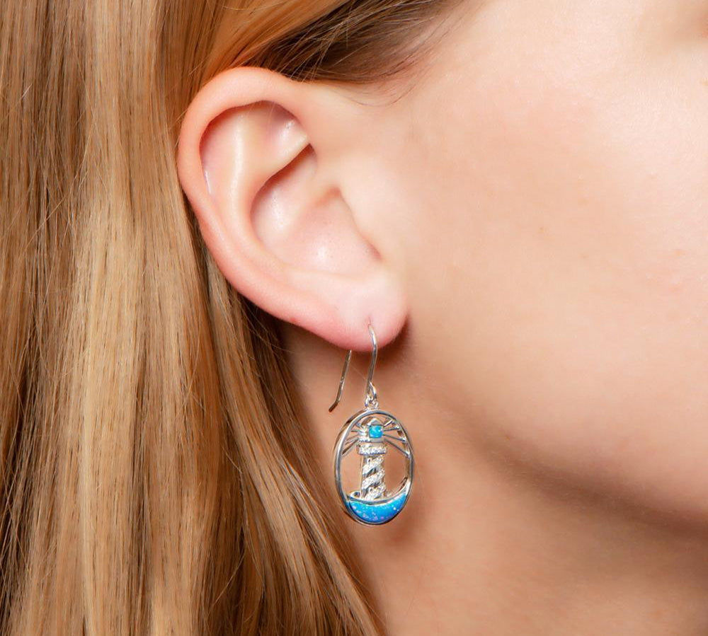 In this photo there is a close-up of a model with blonde hair wearing sterling silver shining lighthouse hook earrings with blue opalite and topaz gemstones.