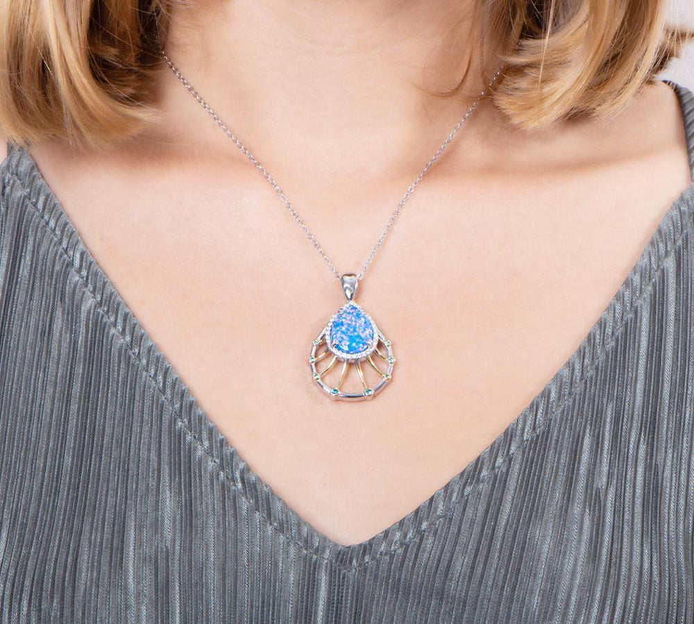 In this photo there is a model with blonde hair and a gray shirt, wearing a sterling silver and gold plated teardrop pendant with blue opalite, aquamarine, and topaz gemstones.