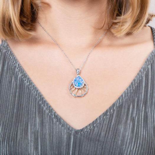In this photo there is a model with blonde hair and a gray shirt, wearing a sterling silver and gold plated teardrop pendant with blue opalite, aquamarine, and topaz gemstones.