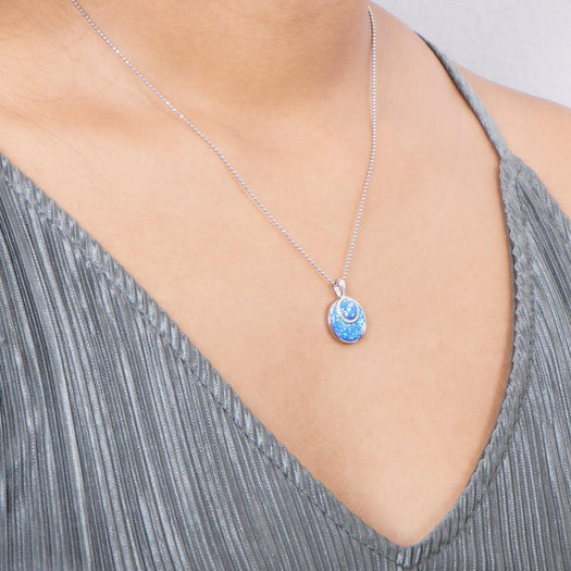 In this photo there is a model with a gray shirt turned slightly to the right, wearing a sterling silver circle pendant with blue opalite and topaz gemstones.