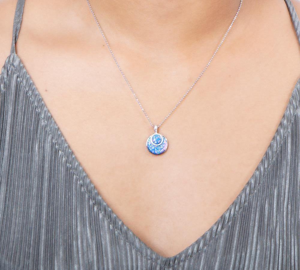 In this photo there is a model with a gray shirt wearing a sterling silver circle pendant with blue opalite and topaz gemstones.