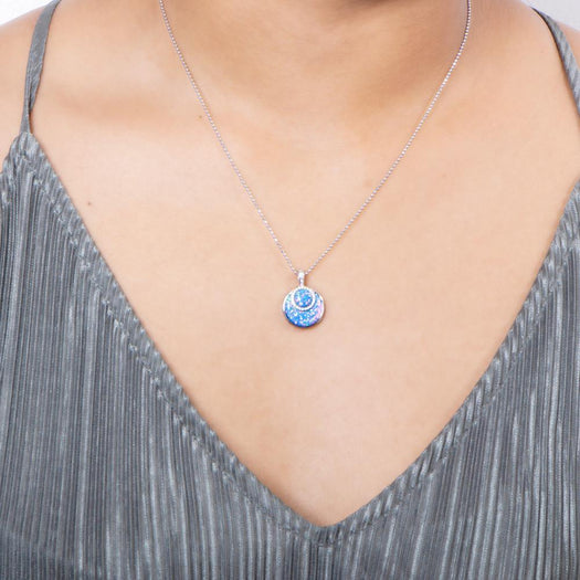 In this photo there is a model with a gray shirt wearing a sterling silver circle pendant with blue opalite and topaz gemstones.