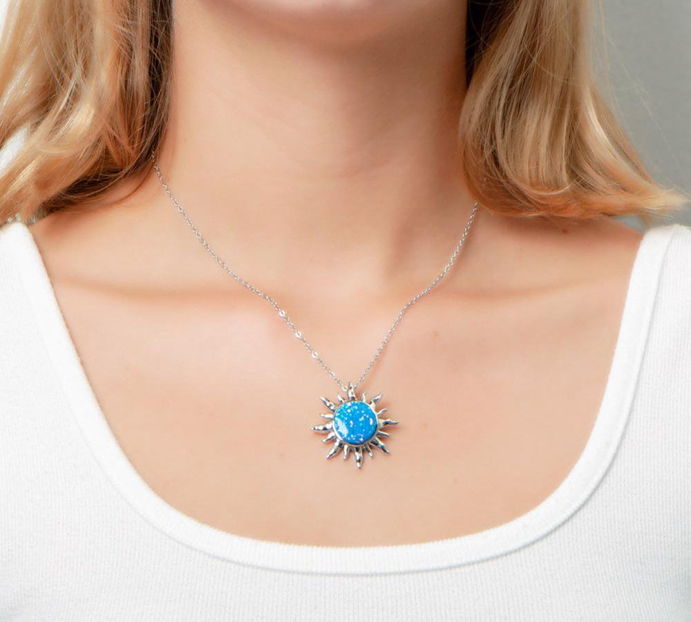 In this photo there is a model with blonde hair and a white shirt, wearing a sterling silver sun pendant with one blue opalite gemstone.