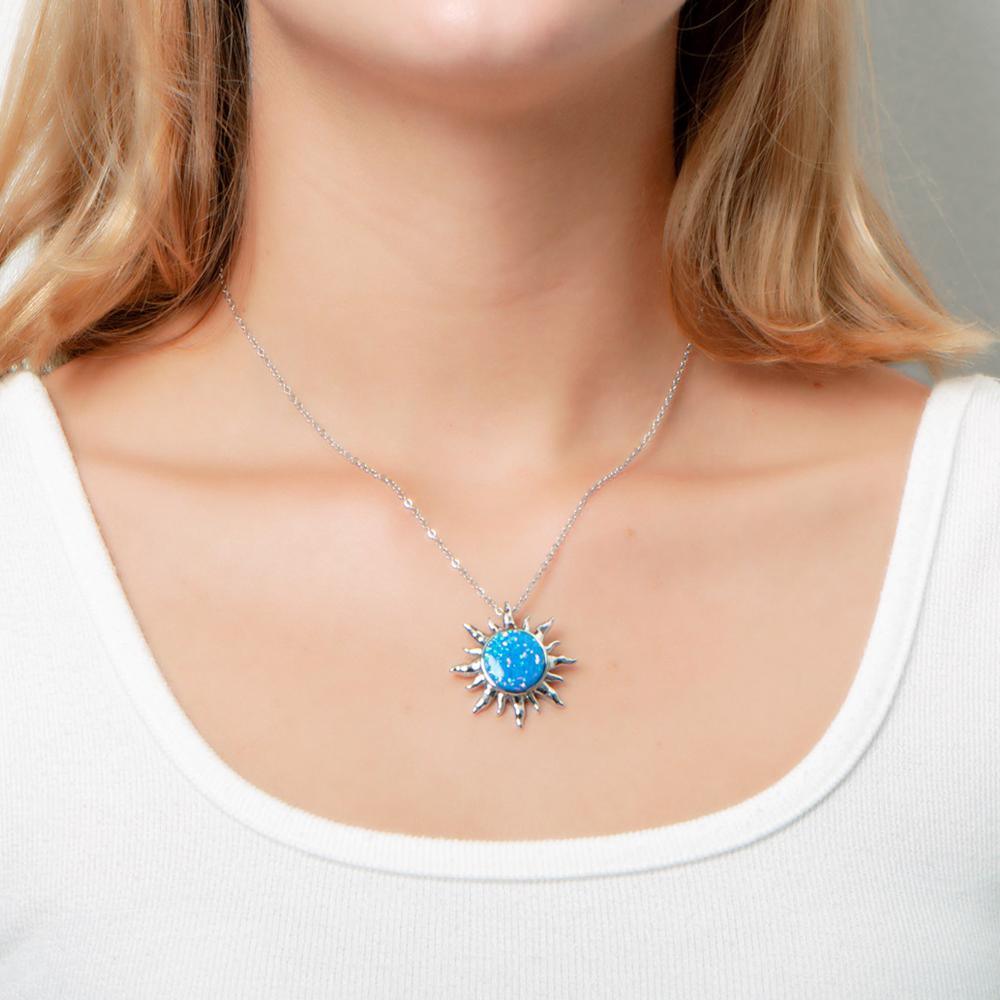 In this photo there is a model with blonde hair and a white shirt, wearing a sterling silver sun pendant with one blue opalite gemstone.