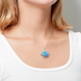 In this photo there is a model turned slightly to the right with blonde hair and a white shirt, wearing a sterling silver sun pendant with one blue opalite gemstone.