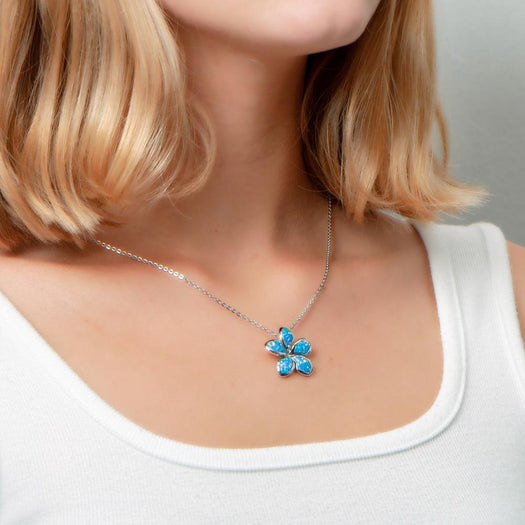 In this picture there is a model faced slightly to the right, with blonde hair and a white shirt, wearing a plumeria pendant with blue opalite set in sterling silver.