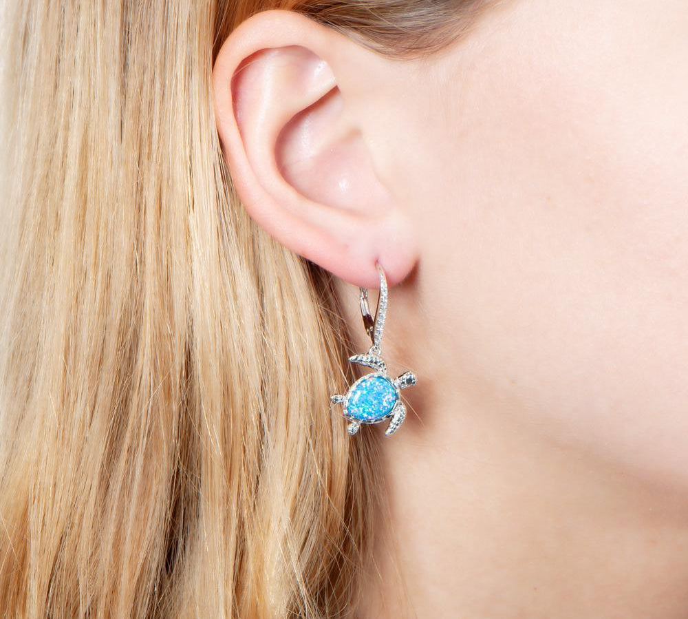 The picture shows a model wearing a 925 sterling silver opalite swimming sea turtle earring with cubic zirconia.