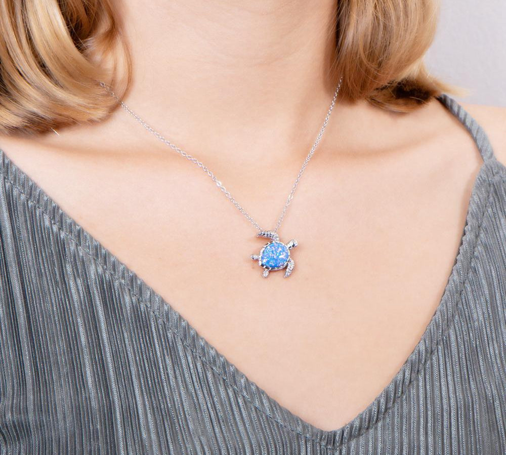 The picture shows a model wearing a 925 sterling silver opalite swimming sea turtle pendant and topaz.