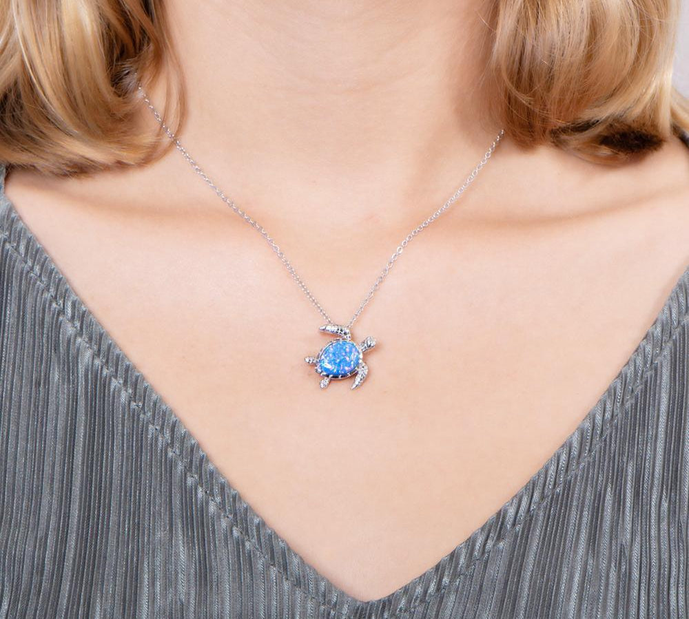 The picture shows a model wearing a 925 sterling silver opalite swimming sea turtle pendant and topaz.