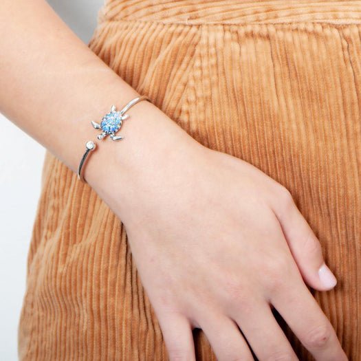 The picture shows a model wearing a 925 sterling silver opalite sea turtle sleek bangle with topaz.