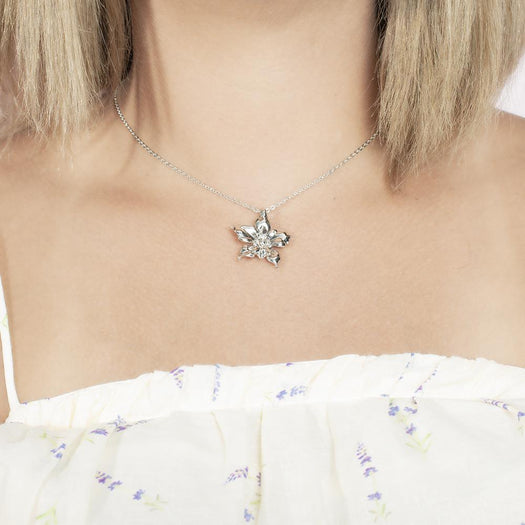 In this photo there is a model with blonde hair and white shirt with purple flowers, wearing a sterling silver orchid pendant.