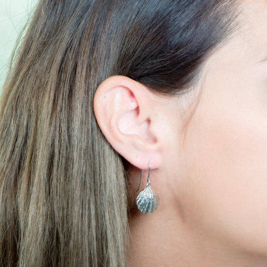 In this picture there is a close-up of a model in profile with brown hair wearing sterling silver oyster shell dangle earrings.