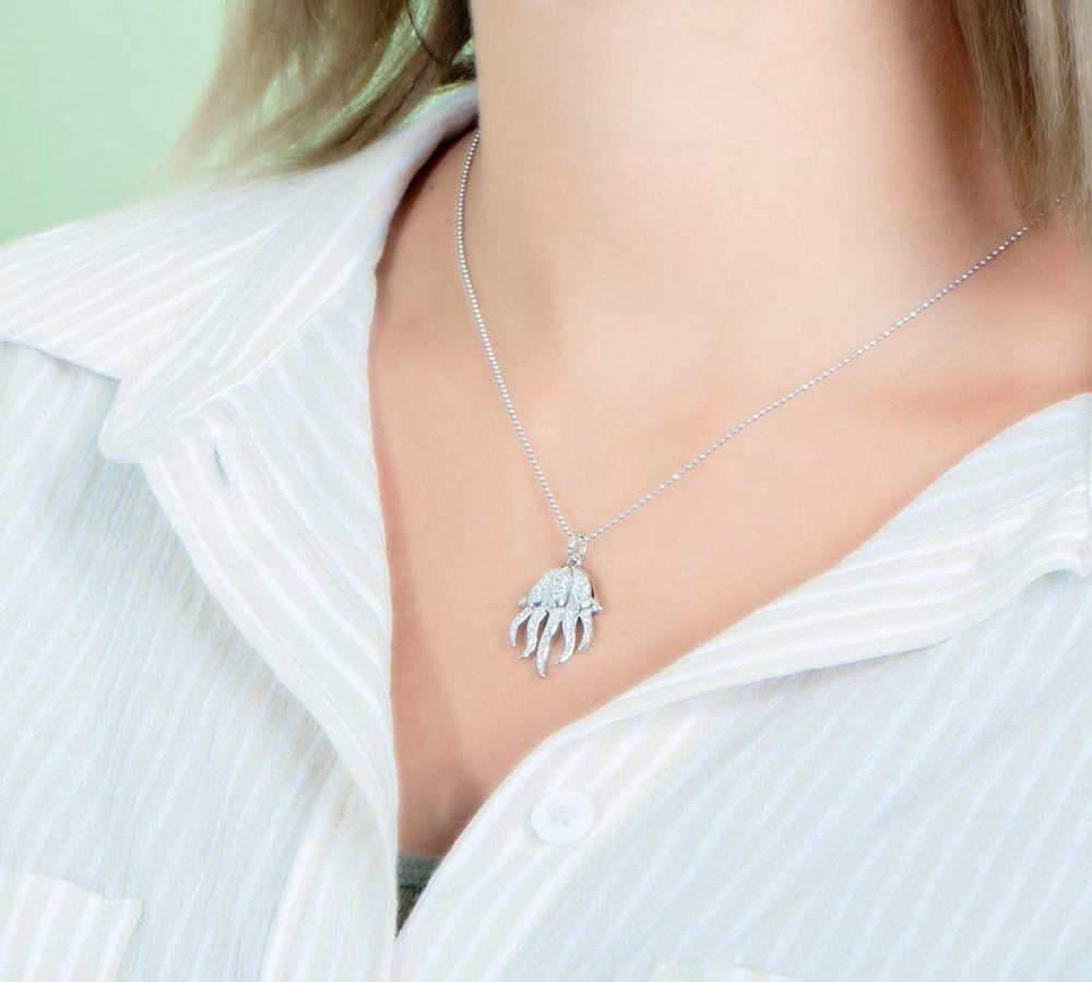 The picture shows a model wearing a 925 sterling silver, white gold plated, pavé barrel jellyfish pendant with topaz.