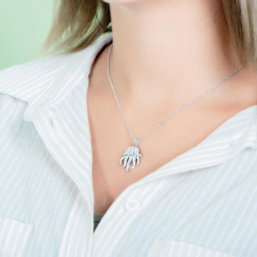 The picture shows a model wearing a 925 sterling silver, white gold plated, pavé barrel jellyfish pendant with topaz.
