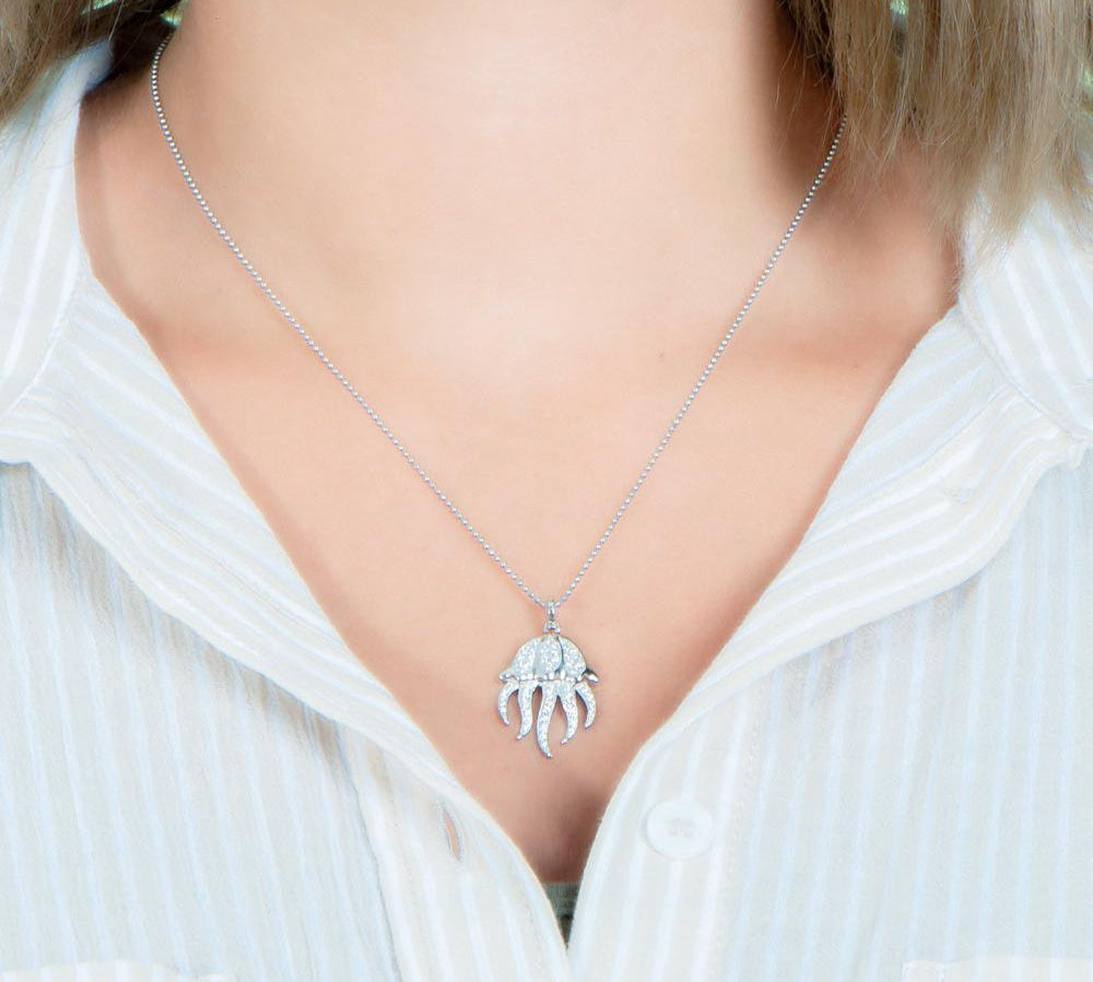 The picture shows a model wearing a 925 sterling silver, white gold plated, pavé barrel jellyfish pendant with topaz.