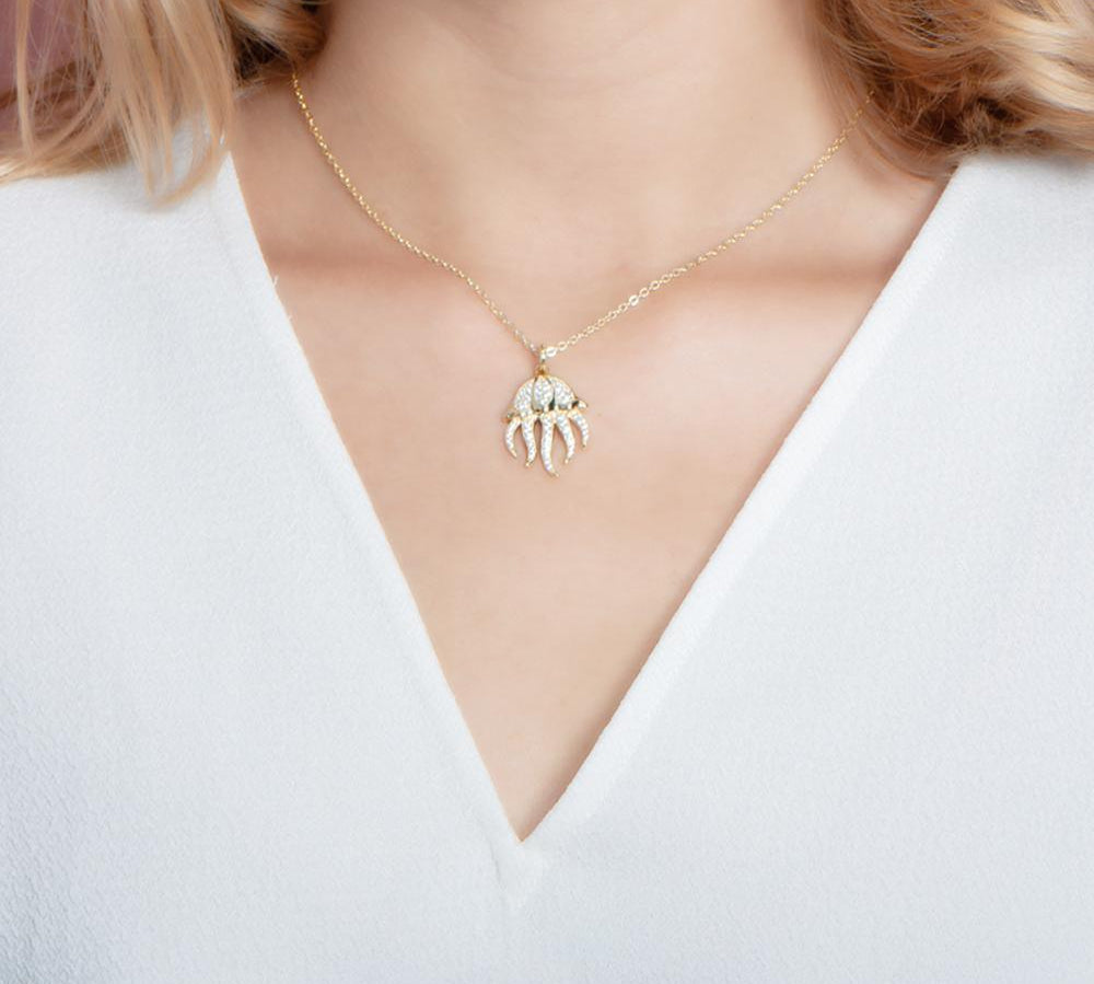 The picture shows a model wearing a 925 sterling silver, yellow gold plated, pavé barrel jellyfish pendant with topaz.