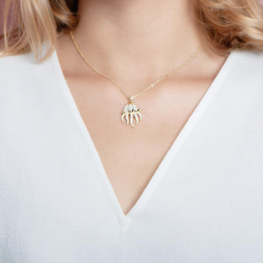 The picture shows a model wearing a 925 sterling silver, yellow gold plated, pavé barrel jellyfish pendant with topaz.