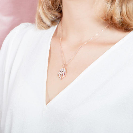 The picture shows a model wearing a 925 sterling silver, rose gold plated, pavé barrel jellyfish pendant with topaz.