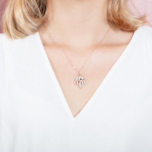 The picture shows a model wearing a 925 sterling silver, rose gold plated, pavé barrel jellyfish pendant with topaz.