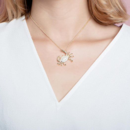 The picture shows a model wearing a 925 sterling silver, yellow gold plated, pavé blue crab pendant with cubic zirconia.