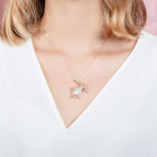 The picture shows a model wearing a 925 sterling silver, rose gold plated, pavé blue crab pendant with cubic zirconia.