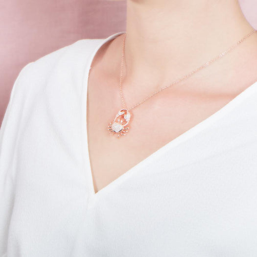 The picture shows a model wearing a 925 sterling silver, rose gold plated, pavé crab pendant with topaz.