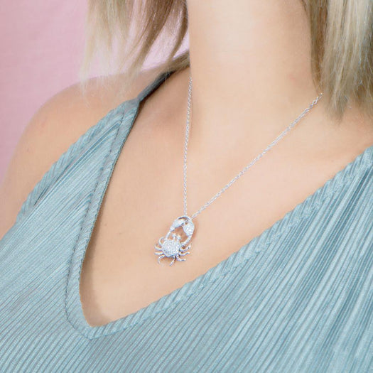 The picture shows a model weaing a 925 sterling silver, white gold plated, pavé crab pendant with topaz.