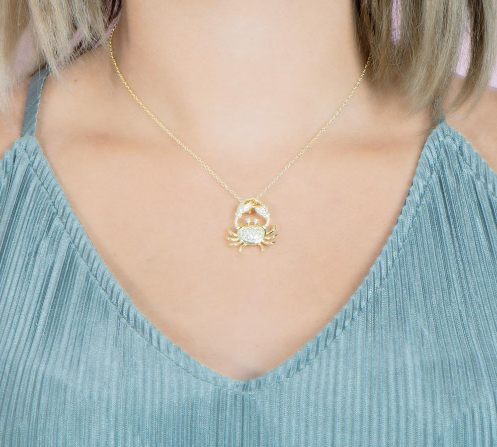 The picture shows a model wearing a 925 sterling silver, yellow gold plated, pavé crab pendant with topaz.