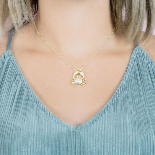 The picture shows a model wearing a 925 sterling silver, yellow gold plated, pavé crab pendant with topaz.