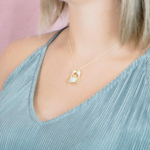 The picture shows a model wearing a 925 sterling silver, yellow gold plated, pavé crab pendant with topaz.